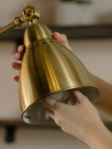 Close-up of hands fixing a light bulb into a modern brass desk lamp, showcasing home maintenance.
