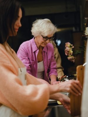 Senior woman in glasses preparing meal with family at home kitchen.